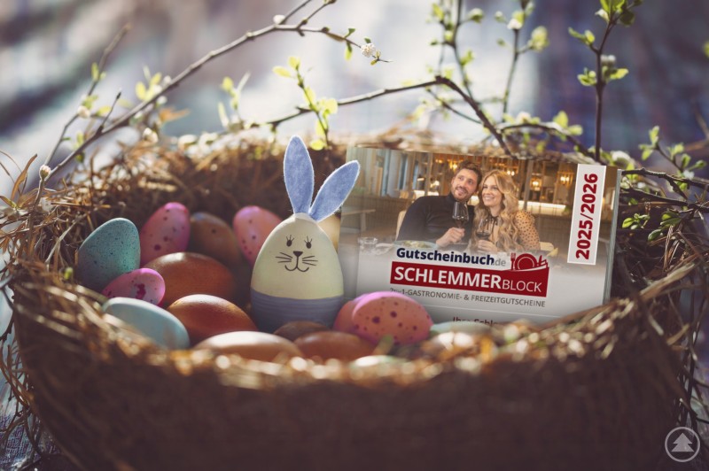 Passt in jedes Osternest: Der Gutscheinbuch.de Schlemmerblock. Ein Osternest mit bunten Eiern, Zweigen und einem dekorativen Hasen, in dem der Gutscheinbuch.de Schlemmerblock platziert ist.