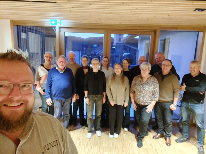 Bürgermeister Robert Bauer (vorne links) holte alle Teilnehmerinnen und Teilnehmer des Rusel-Gipfeltreffens zum Gruppenfoto zusammen. Eine Gruppe von Vertreterinnen und Vertretern aus Gemeinden, Tourismus und Vereinen steht gemeinsam in einem Gastraum und blickt lächelnd in die Kamera. Im Vordergrund ist der Gastgeber zu sehen, der ein Selfie aufnimmt.