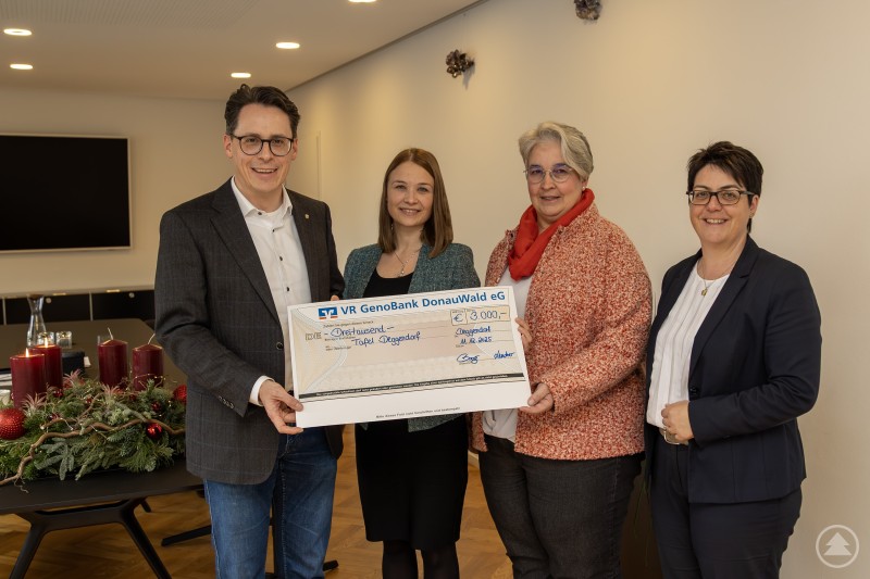 v. l.: Oberbürgermeister Dr. Christian Moser, Natalie Berger (Geschäftsstellenleiterin), Christiane Preiß (Bürgerarbeit der Stadt Deggendorf) und Anita Linzmeier (Vorständin) Vier Personen stehen in einem festlich geschmückten Raum und halten gemeinsam einen symbolischen Spendenscheck der VR GenoBank DonauWald eG in den Händen. Alle Beteiligten lächeln in die Kamera, im Hintergrund ist ein Tisch mit Adventsdekoration zu sehen.