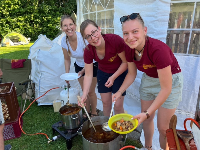 Drei junge Frauen geben draußen auf Tellern Essen an Kinder aus