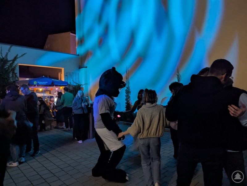 Zu pulsierender DJ-Musik tanzten die Gäste und THD-Maskottchen Deggster bis spät in die Nacht. THD-Maskottchen Deggster tanzt mit Gästen auf der blau beleuchteten Tanfläche