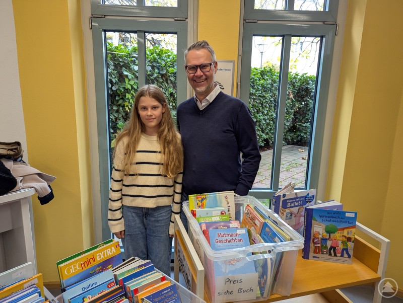 Das Schöne an (Bücher-)Flohmärkten: Es ergeben sich neben tollen Kaufgelegenheiten immer auch nette Gespräche. Mädchen und Vater lächeln am Flohmarktstand in die Kamera