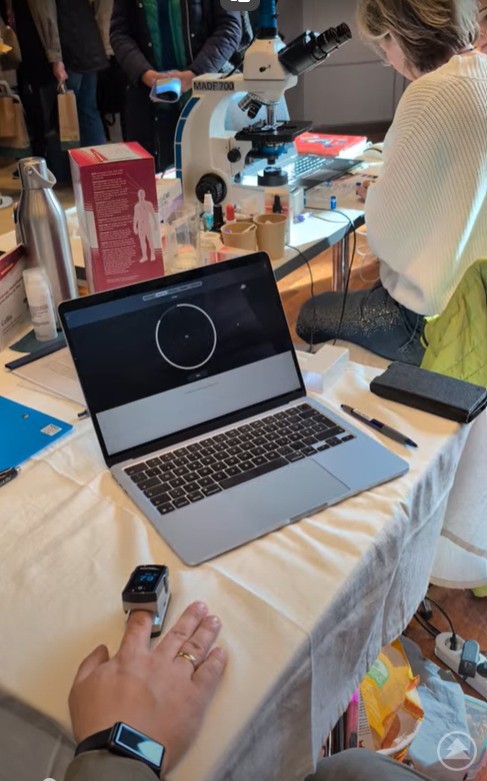 Verschiedene Tests konnten direkt vor Ort durchgeführt werden Ein Laptop zeigt die Auswertung eines Puls- und Arterienmessgerätes, im Hintergrund sitzt eine Frau am Mikroskop und macht Bluttests
