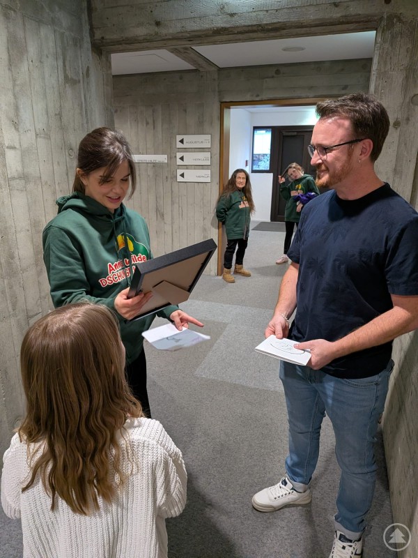 Portraitzeichner Florian Eibl übergibt Annika Preil ihr persönliches Portrait Mädchen übergibt ein gerahmtes Portrait an eine Frau während ein Mann daneben steht