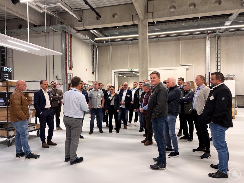 Die Gruppe der Mittelstandsunion Freyung-Grafenau besichtigt die neuen Räumlichkeiten der Thomas-Krenn.AG. Eine Gruppe von Besucherinnen und Besuchern steht gemeinsam mit einem Firmenvertreter in einer modernen Produktionshalle. Im Hintergrund sind Maschinen, Regale und technische Anlagen zu sehen. Der Firmenvertreter erklärt Details zum Produktionsablauf.