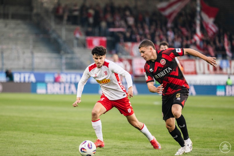 Ein Spieler des SSV Jahn im weißen Trikot kämpft im Laufduell mit einem Wiesbadener Spieler um den Ball.