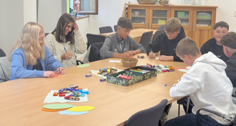 Eine Gruppe Jugendlicher arbeitet gemeinsam an einem Tisch an Ideen und Vorschlägen, auf dem Süßigkeiten und bunte Papierkarten liegen.