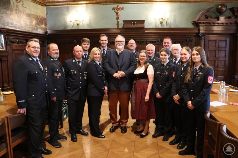 Schirmherrenbitte im kleinen Rathaussaal: Oberbürgermeister Jürgen Dupper (Mitte) mit Fahnenmutter Bettina Sturm (7. von rechts), Kommandant Otto Neiß (6. von rechts), Vorstand Markus Frank (8. von rechts) sowie weitere Vertreter der Freiwilligen Feuerwehr Grubweg e.V. Das Bild zeigt eine Gruppe von Feuerwehrangehörigen der Freiwilligen Feuerwehr Grubweg gemeinsam mit Passaus Oberbürgermeister Jürgen Dupper in einem historischen Sitzungssaal. Die Mitglieder tragen festliche Uniformen, einige Abzeichen und Auszeichnungen sind sichtbar. In der Mitte steht OB Dupper neben einer Frau in traditioneller Tracht. Die feierliche Atmosphäre sowie die würdige Kulisse mit Holzvertäfelung, Kruzifix und Wandgemälden deuten auf einen besonderen Anlass hin – vermutlich die Übernahme der Schirmherrschaft durch den Oberbürgermeister anlässlich des 140-jährigen Jubiläums der Feuerwehr Grubweg. Die Stimmung ist feierlich und geprägt von Stolz und Gemeinschaft.