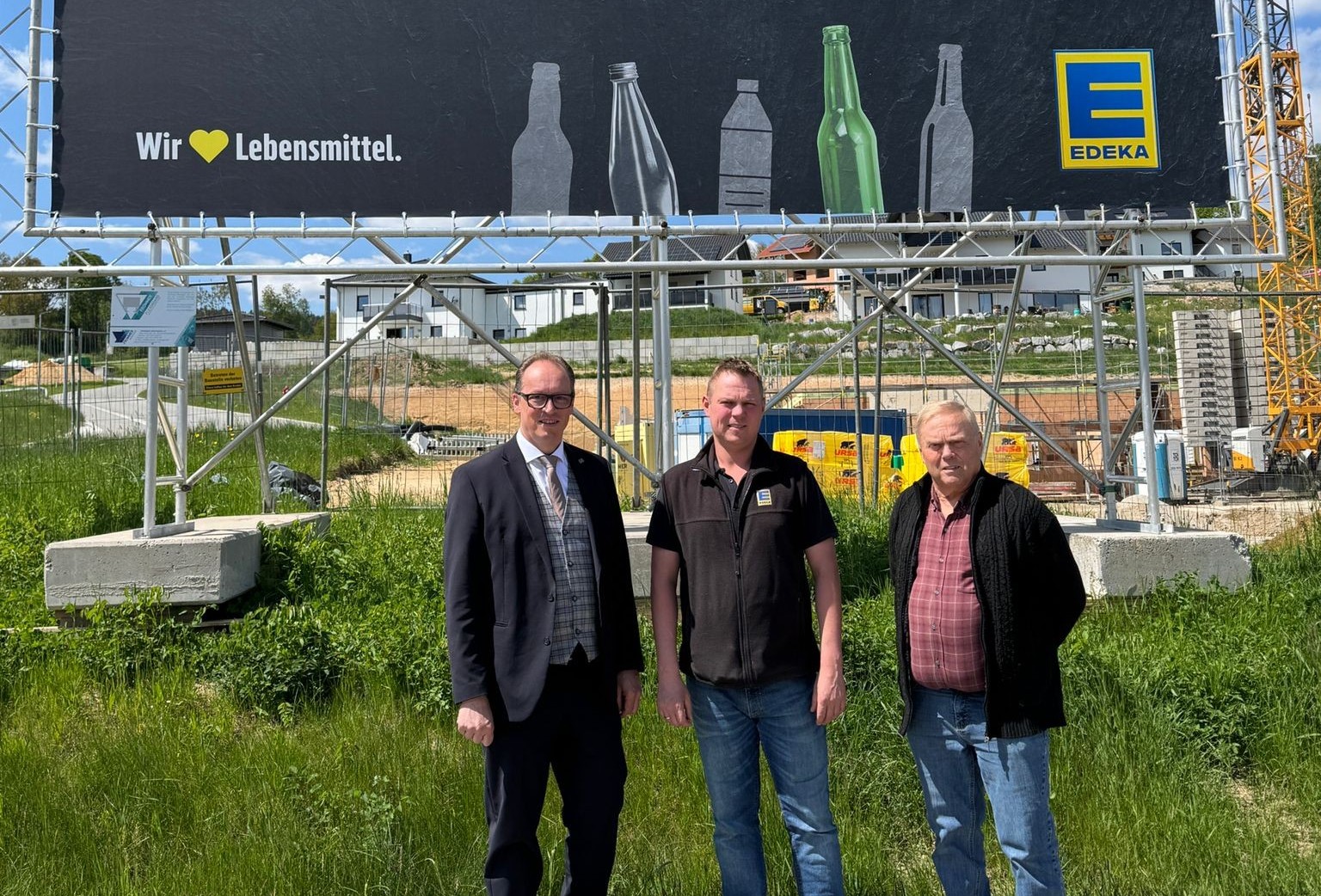 MdL Martin Behringer (links) zu Besuch bei EDEKA Kauer in Teisnach. Neben ihm die Betreiber des Marktes vor dem Baustellenschild des neuen Getränkemarkts. Landtagsabgeordneter Martin Behringer und die Betreiber von EDEKA Kauer stehen vor einem großen Baustellenschild