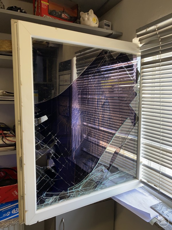 Rabiat drangen die Einbrecher in Wohn- und Geschäftsräume ein. Eine Fensterscheibe eines Gebäudes ist komplett zersplittert, Glasreste liegen auf der Fensterbank, im Hintergrund ist ein Büroregal zu sehen.