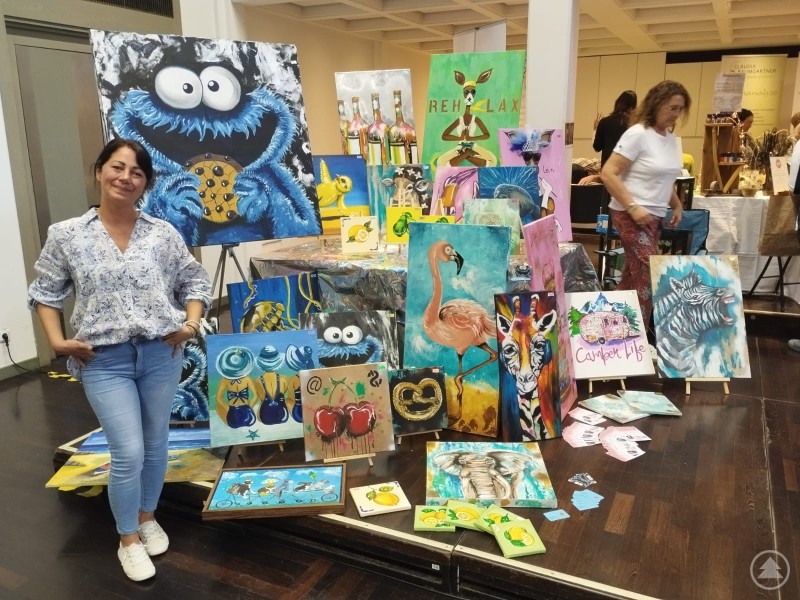 Nicole Forster mit einigen ihrer Werke auf der Frauenmesse in Dingolfing Nicole Forster steht an ihrem Messestand, wo viele Staffeleien und Tische mit ihren Bildern präsentiert werden.