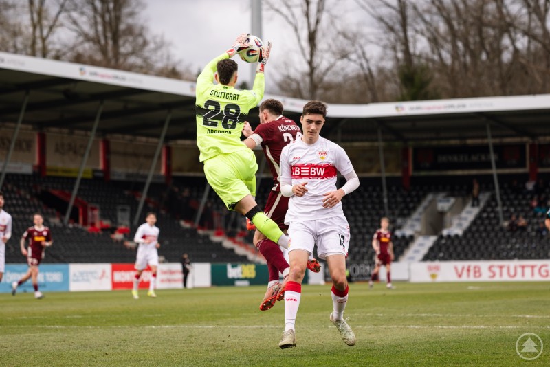 Ein Torwart springt hoch und f&auml;ngt den Ball, w&auml;hrend Spieler beider Mannschaften im Strafraum um die Szene k&auml;mpfen