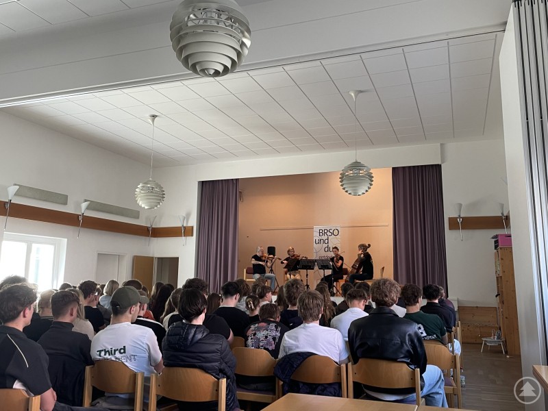 Ein Streichquartett des Symphonieorchesters des Bayerischen Rundfunks begeistert die Schülerinnen und Schüler des LLG Grafenau. Ein Saal mit vielen sitzenden Schülerinnen und Schülern, die einer Aufführung eines Streichquartetts auf einer kleinen Bühne aufmerksam zuhören.