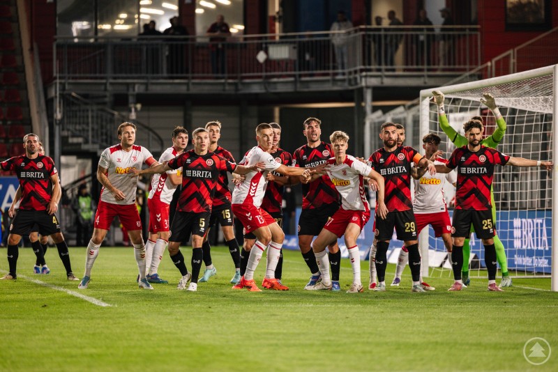 In den Strafraumszenen fehlte dem Jahn die letzte Durchschlagskraft, um ein Tor zu erzielen. Spieler beider Mannschaften stehen eng gedrängt im Strafraum und bereiten sich auf eine Standardsituation vor.