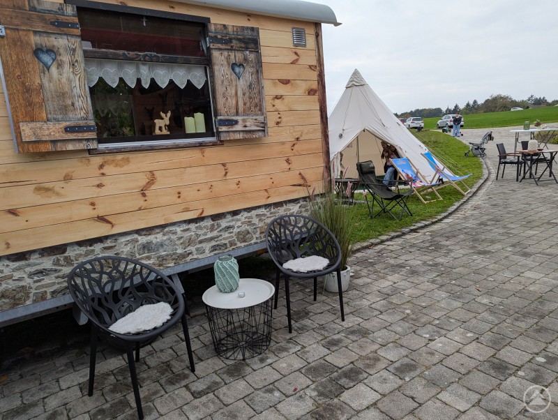 Ankommen und die Seele baumeln lassen heißt es im Hofcafé, das jeden letzten Sonntag im Monat für alle geöffnet ist. Zwei Stühle und Stahltisch vor Holzwohnwagen und weißem Zelt