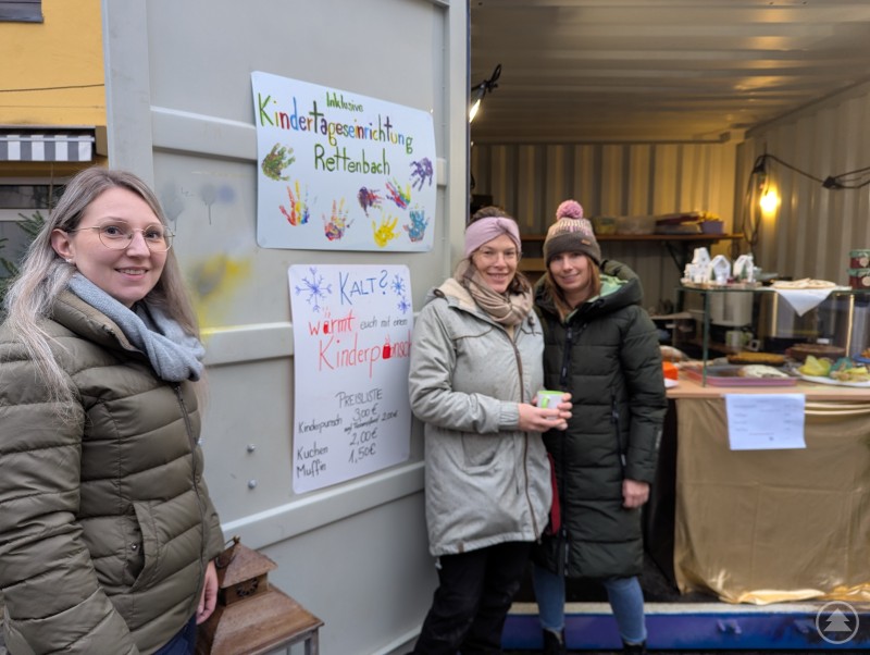 Die Inklusive Kindertageseinrichtung Rettenbach hatte u.a. köstlichen Kuchen und wärmenden Kinderpunsch mitgebracht. Drei Mitarbeiterinnen der Inklusiven Kindertageseinrichtung Rettenbach lächeln in die Kamera
