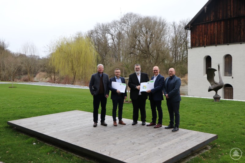 Bürgermeister Andreas Rother (3. von rechts) gratuliert Dr. Markus Pfaffinger (2. v. rechts) und (v. r.) Niklas Kolmer sowie Severin Widera und Michael Häring von der Pfaffinger Unternehmensgruppe für die erfolgreiche Teilnahme am Umwelt- und Klimapakt Bayern.Bürgermeister Andreas Rother (3. von rechts) gratuliert Dr. Markus Pfaffinger (2. v. rechts) und (v. r.) Niklas Kolmer sowie Severin Widera und Michael Häring von der Pfaffinger Unternehmensgruppe für die erfolgreiche Teilnahme am Umwelt- und Klimapakt Bayern. Fünf Männer bei einer Urkundenübergabe im Freien vor einem Gebäude und Parkanlage