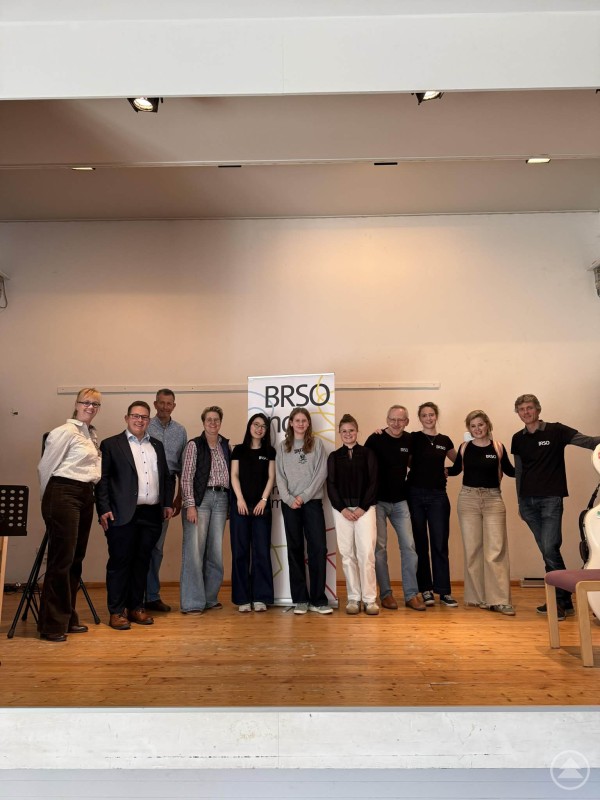 Die Musiker des BR-Symphonieorchesters zusammen mit Organisatoren und Gästen nach der Veranstaltung in Grafenau. Mehrere Musikerinnen und Musiker sowie Organisatoren stehen gemeinsam auf einer Bühne und posieren für ein Gruppenfoto vor einem Banner des BR-Symphonieorchesters.
