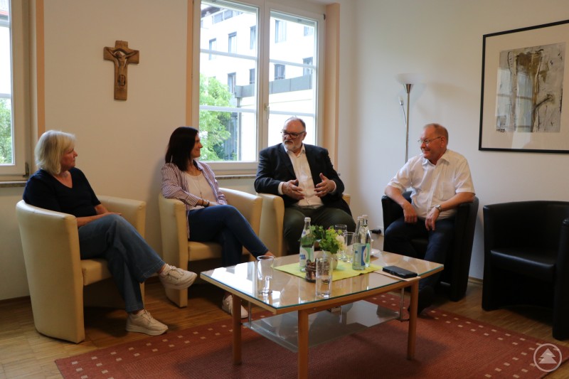 Oberbürgermeister Jürgen Dupper (2. v. rechts) im Gespräch mit (v. r.) Pater Ludger Werner, Sabine Müller und Marianne Kopfinger anlässlich des 50-jährigen Jubiläums der Telefonseelsorge Passau. Vier Personen sitzen in einem hellen Raum mit großen Fenstern in einer Gesprächsrunde. Auf dem Tisch stehen Wasserflaschen, Gläser und eine Blumendekoration. Ein Holzkreuz hängt an der Wand, es herrscht eine ruhige und offene Gesprächsatmosphäre.