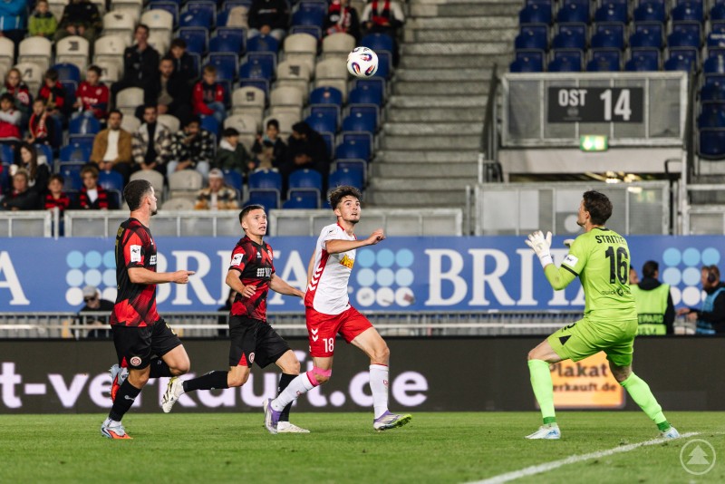 Auch in der Offensive blieb der Jahn glücklos – selbst beste Chancen führten nicht zum Torerfolg. Ein Jahn-Spieler läuft auf den Wiesbadener Torhüter zu, während dieser den Ball erwartet und zwei Abwehrspieler zurücklaufen.