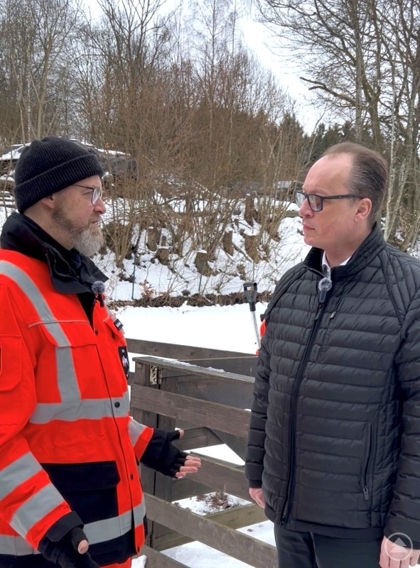 Vorsitzender der Rettungshundestaffel Bayerischer Wald e.V., Martin Duckstein (l.) freut sich, dass mit der Hilfe auf Vermittlung von MdL Martin Behringer Ausstattung für die zahlreichen Einsätze leichter angeschafft werden kann. Am Trainingsgelände bei Kumreut gab es noch zu Winterzeiten ein Gespräch über Arbeit und Aufwand der Staffel. Zwei Männer stehen im Winter auf einem Trainingsgelände der Rettungshundestaffel im Gespräch. Einer trägt eine auffällige orange Rettungsjacke, der andere eine schwarze Jacke. Im Hintergrund sind verschneite Bäume zu sehen.