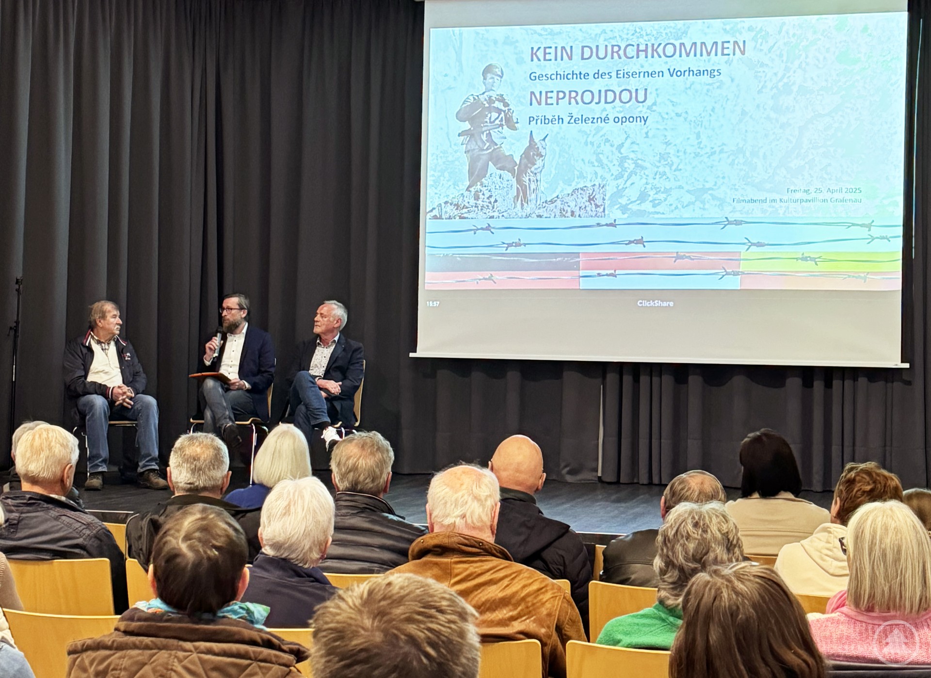 Eine Gruppe von Teilnehmenden sitzt aufmerksam beim Zeitzeugengespräch nach der Filmvorführung. Christian Fiebig spricht mit Miroslav Dudycha und Siegfried Schreindl.