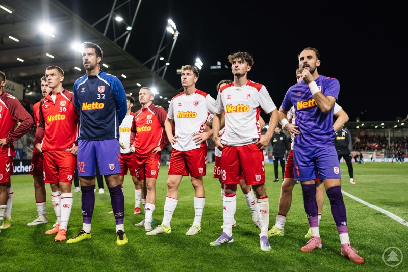 Ernüchterung nach Abpfiff: Die Jahnelf kassierte in Wiesbaden die nächste Niederlage und zeigte sich selbstkritisch. Spieler des SSV Jahn Regensburg stehen nach dem Spiel enttäuscht auf dem Rasen, einige mit verschränkten Armen, andere mit nachdenklichen Blicken.