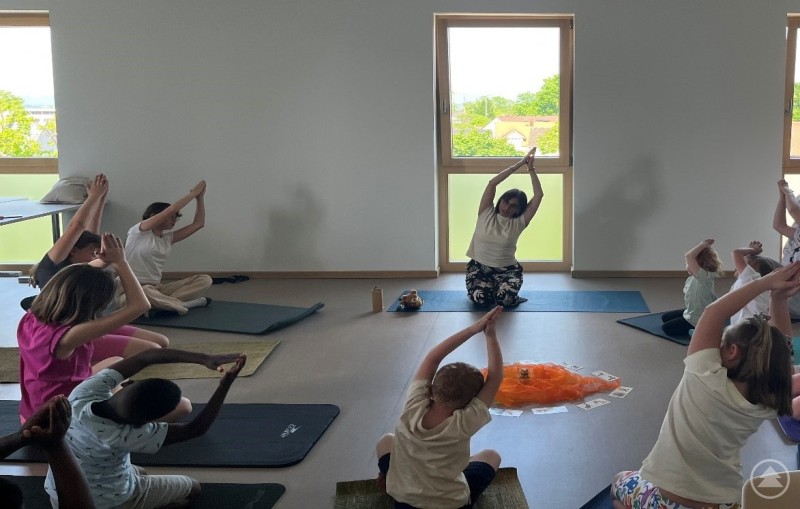 Pflegekinder erleben eine entspannende Yogastunde im Landratsamt Straubing-Bogen. Eine Gruppe von Kindern und Jugendlichen praktiziert Yoga unter Anleitung einer Yogalehrerin in einem hellen Raum.