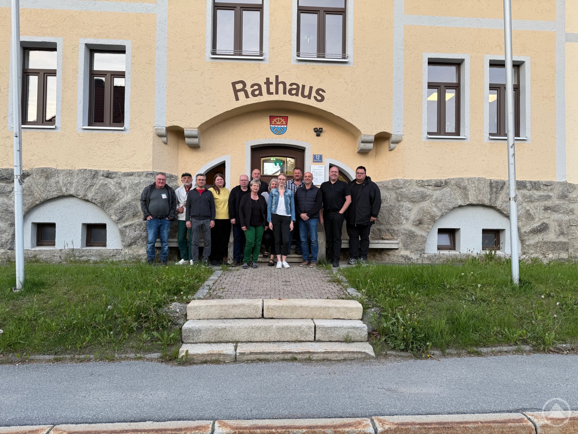 Eine Gruppe von Personen steht vor dem Rathaus in Haidmühle und posiert für ein gemeinsames Foto. Das historische Gebäude im Hintergrund ist gelb und hat einen Schriftzug „Rathaus“ über dem Eingang.