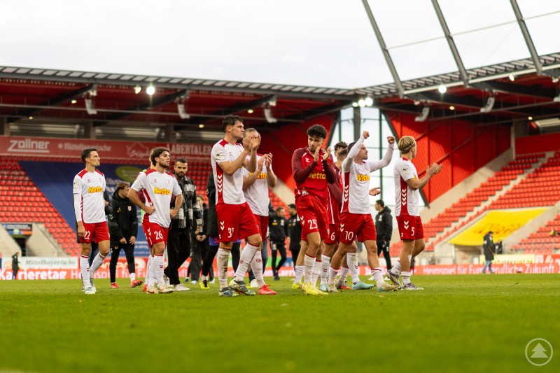 Mannschaftsapplaus nach dem Spiel Regensburger Spieler stehen gemeinsam auf dem Feld und klatschen Richtung Tribüne.