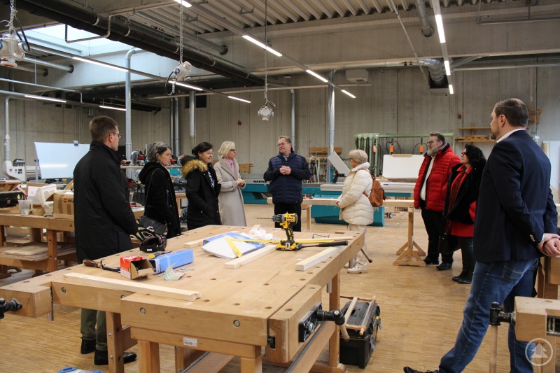 In der Bildmitte Josef Sailer (Leiter des Bildungszentrums) bei der Erklärung des Arbeitsbereiches der Tischler/innen Ein Gruppenrundgang in einer modernen Werkstatt mit Werkbänken, Maschinen und Werkzeugen. Josef Sailer, der Leiter des Bildungszentrums, steht in der Bildmitte und erklärt den Arbeitsbereich der Tischlerinnen und Tischler. Die Gruppe hört aufmerksam zu.