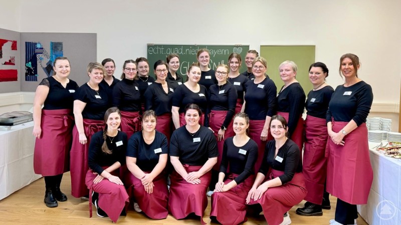 Mit dem Abschlussbuffet „Echt.Guad.Niederbayern.“ verabschiedeten sich die 24 Studierenden der Landwirtschaftsschule Passau, Abteilung Hauswirtschaft, von ihrer Schulzeit. Eine Gruppe von Frauen in einheitlicher Kleidung steht gemeinsam für ein Gruppenfoto in einem Raum.