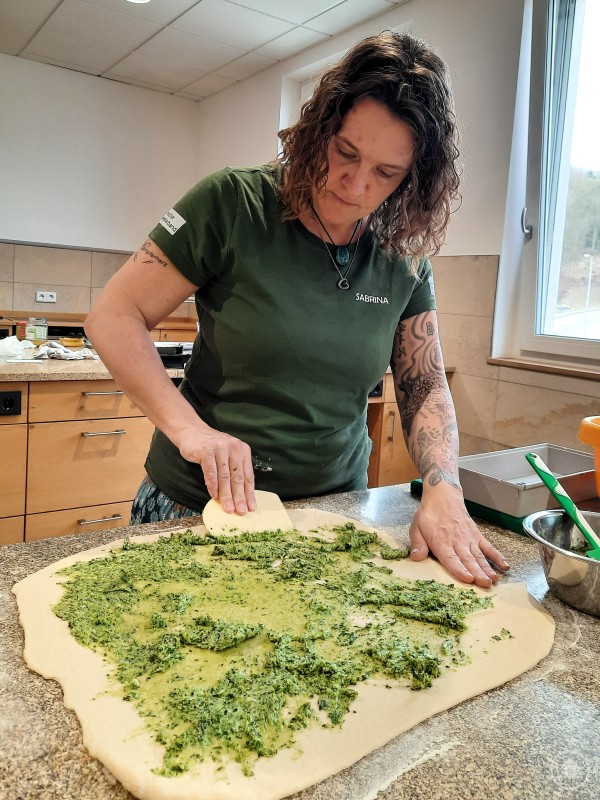 Sabrina Danböck bereitet ein Bärlauch Zupfbrot zu Frau bereitet in einer Küche einen Teig mit grüner Kräuterfüllung zu