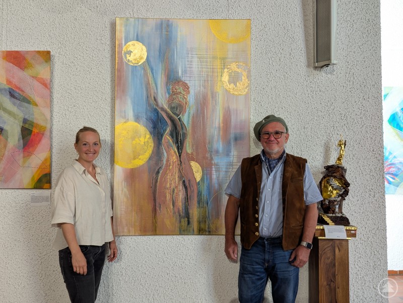 Lisa Pielmeier und Dieter Speth lächeln vor Gemälde in die Kamera