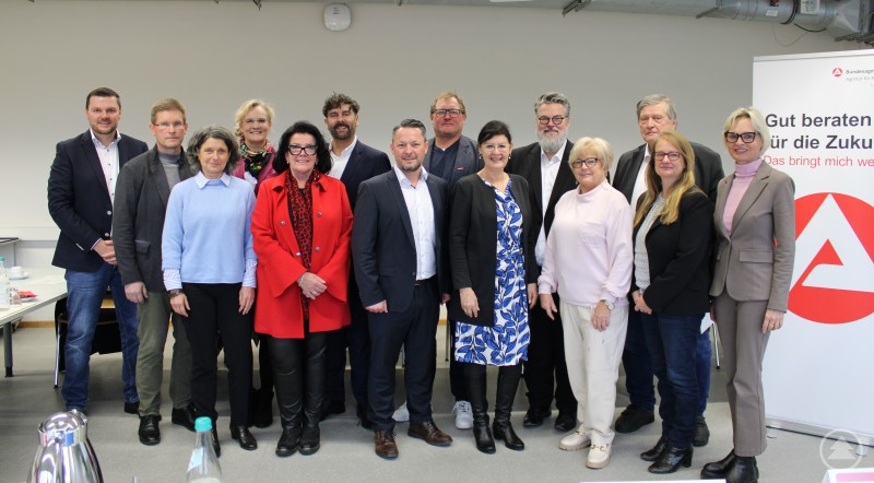 Von links: Michael Mautner, Rüdiger Kindermann, Roswitha Berge, Dr. Jutta Krogull, Marion Korn, Tobias Cziudaj, Alexander Eder, Christian Erntl, Eva-Maria Kelch (Leiterin der Agentur für Arbeit Passau), Andreas Rother, Helga Weinberger, Klaus Jeggle, Bettina Blöhm (Vorsitzende des Verwaltungsausschusses), Cornelia Wasner-Sommer Eine Gruppe von 15 Frauen und Männern steht gemeinsam für ein Gruppenfoto vor einem neutralen Hintergrund, rechts ist ein Roll-up der Agentur für Arbeit Passau mit dem Slogan „Gut beraten für die Zukunft“ zu sehen. Die Stimmung ist freundlich und professionell.