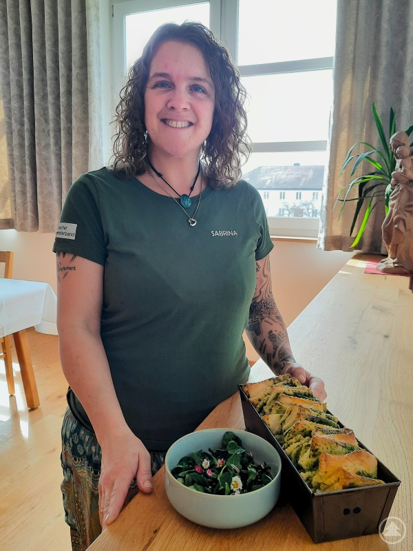 Sabrina Danböck zeigt das fertige Bärlauch Zupfbrot und den Wildkräutersalat Frau präsentiert fertiges Bärlauch Zupfbrot und einen Wildkräutersalat in einer Küche