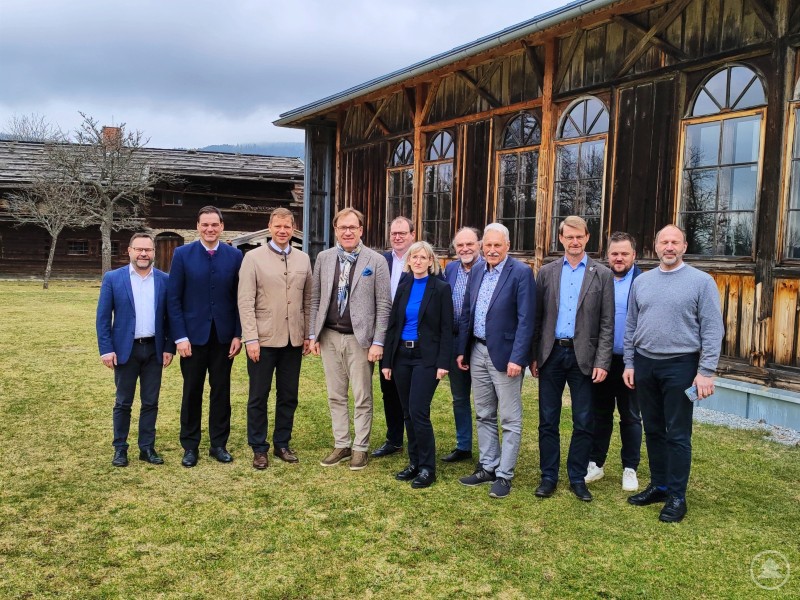 Die Verbandsversammlung des Zweckverbandes Niederbayerische Freilichtmuseen Massing im Rottal und Finsterau im Bayerischen Wald tagte unlängst im Freilichtmuseum Finsterau: (von links nach rechts) Bezirksrat Stephan Gawlik, Landrat Sebastian Gruber (Freyung-Grafenau), Bezirkstagspräsident Dr. Olaf Heinrich, Bezirkstagsvizepräsident Dr. Thomas Pröckl, Landrat Michael Fahmüller (Rottal-Inn), Betriebsleiterin Stephanie Herzig, Bezirksrat Rolf-Peter Holzleitner, Stiftungsvorsitzender Josef Auer (Stiftung Niederbayerisches Bauernhofmuseum Massing), 2. Bürgermeister Georg Obermaier (Massing), Bürgermeister Heiner Kilger (Mauth) und Museumsleiter Timm Miersch. Eine Gruppe von zwölf Personen steht draußen vor einem Holzgebäude. Sie tragen Business- oder Freizeitkleidung, und das Wetter ist bewölkt