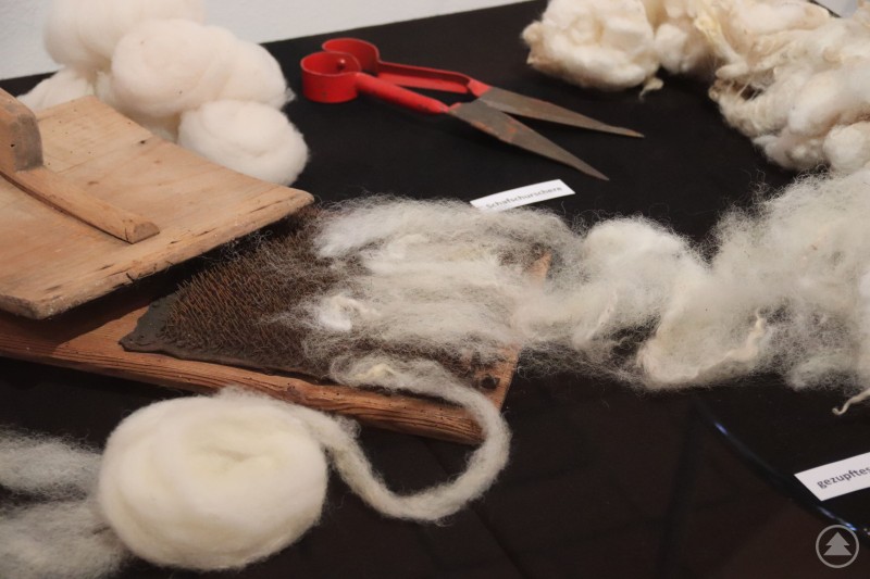 Ausstellungsstücke der Sonderausstellung zum Thema „Spinnst Du“ Verschiedene Exponate zur Textilherstellung, darunter Schafwolle und Werkzeuge zur Verarbeitung.