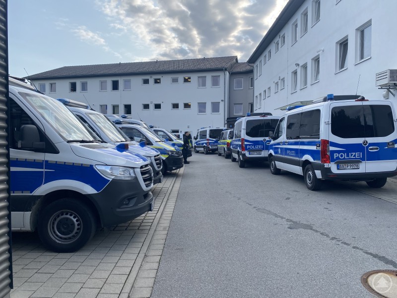 Polizeipräsenz bei der Begehung der Unterkunft in Hengersberg am Leebbergheim. Mehrere Polizeibusse stehen dicht aneinandergereiht in einem Innenhof vor einem weißen Gebäude.