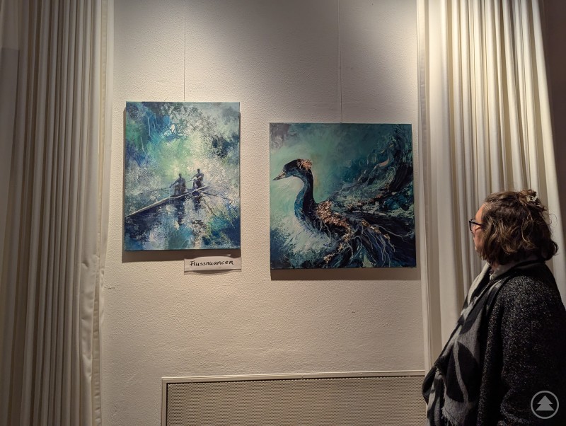 Hier ist der genaue Blick gefragt: Eine Besucherin lässt zwei Bilder von Susanne Sikora auf sich wirken. Ausstellungsbesucherin betrachtet zwei blaue Gemälde von Susanne Sikora