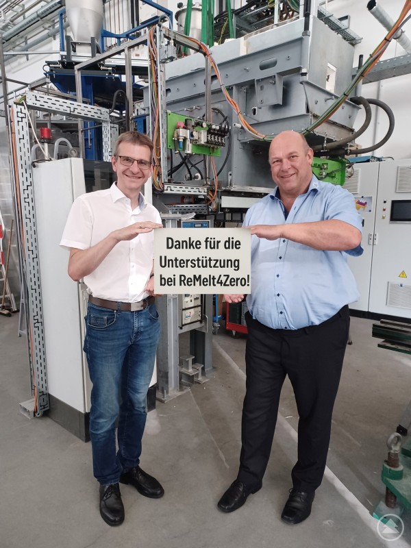 Freuen sich über die Bewilligung der Forschungsmittel und übermitteln der Landespolitik ihren Dank: Spiegelaus Bürgermeister Karlheinz Roth (li.) und der wissenschaftliche Leiter des TAZ Spiegelau Prof. Harald Zimmermann (re.). Zwei Männer stehen vor einer technischen Versuchsanlage und halten ein Schild mit der Aufschrift „Danke für die Unterstützung bei ReMelt4Zero!“