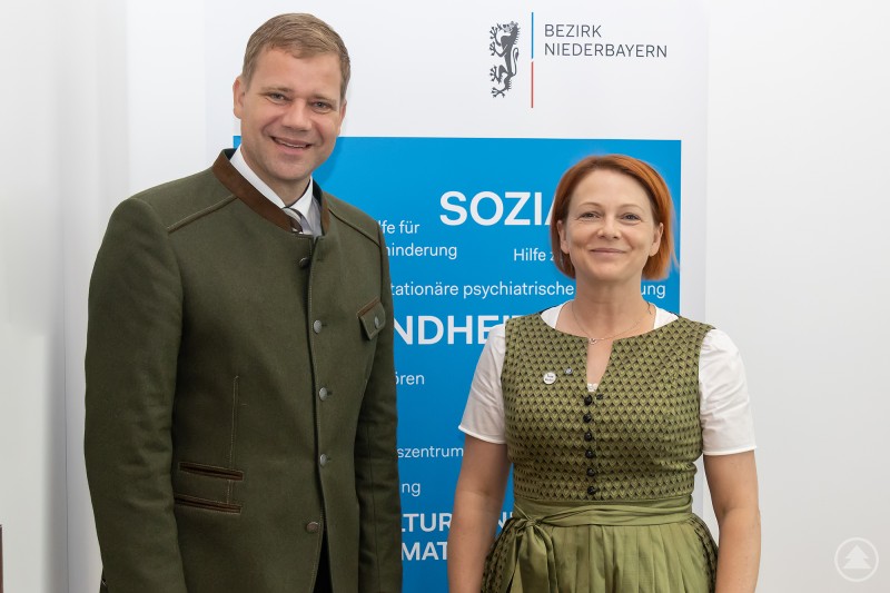 Bezirkstagspräsident Dr. Olaf Heinrich und MdL Mia Goller tauschten sich über Regionalität und Versorgungssicherheit aus. Eine Frau und ein Mann stehen nebeneinander vor einem Roll-up mit dem Logo „Bezirk Niederbayern“. Beide lächeln freundlich in die Kamera. Der Mann trägt eine traditionelle grüne Tracht, die Frau ein grünes Dirndl. Die Aufnahme wirkt professionell und zeigt eine positive Gesprächsatmosphäre.