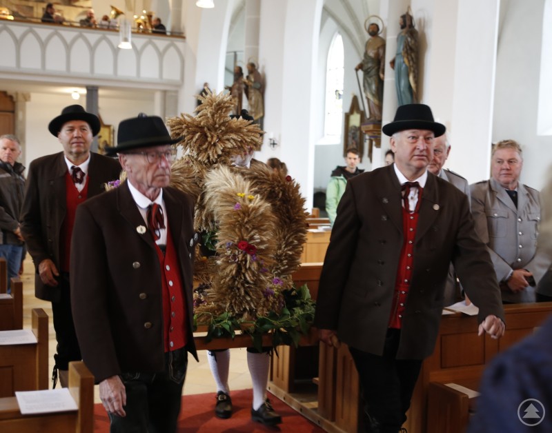 Eine festlich geschmückte Erntekrone wurde in den Altarraum getragen und dort feierlich gesegnet. Mitglieder des Heimat- und Volkstrachtenvereins tragen in traditioneller Kleidung eine große Erntekrone durch den Mittelgang der Kirche.