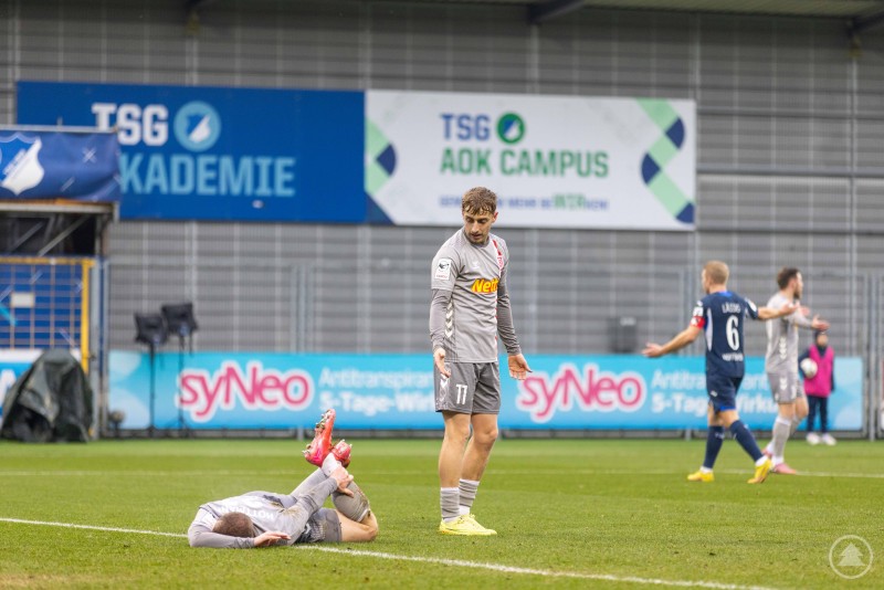 Ein liegender Jahn-Spieler am Boden, während ein Mitspieler besorgt reagiert.