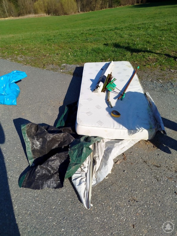 Hat da jemand seinen Haushalt aufgelöst? Eine saubere Umwelt braucht eigentlich keinen Wischer! Und zur gemütlichen Pause lädt eine feuchte Matratze auch gerade nicht ein. Am Rand eines Feldwegs liegt illegal entsorgter Sperrmüll. Eine alte Matratze, Planen und verschiedene Gegenstände wurden einfach in der Natur abgelegt. Im Hintergrund sind eine Wiese und ein Waldrand zu sehen.