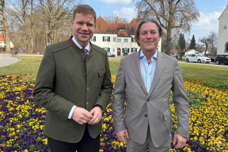 Bezirkstagspräsident Dr. Olaf Heinrich traf sich mit Prof. Dr. Joachim Nitschke in der Verwaltung des Bezirksklinikums Mainkofen zum Jahresgespräch. Zwei Männer stehen vor einem blühenden Blumenbeet im Freien. Im Hintergrund ist ein Gebäude des Bezirksklinikums zu sehen.
