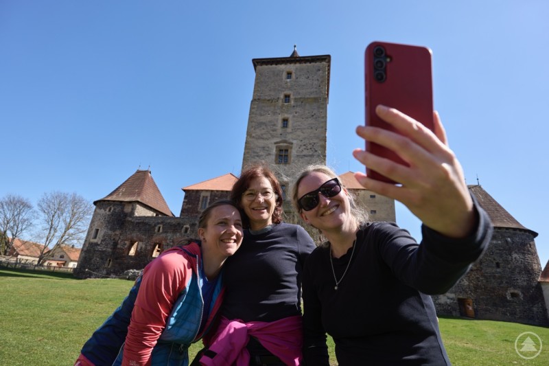 Besucher genießen ihren Ausflug zur Aschenbrödel-Burg Švihov mit dem BöhmerwaldCourier. Drei Frauen machen ein Selfie vor der historischen Burg Švihov bei sonnigem Wetter.