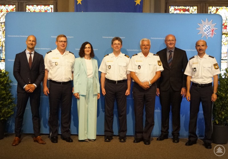 v.l.n.r.: KOR DR. Erik Stegner, PD Christian Dichtl, RDin Ellen Wagner, PP Roland Kerscher, PVP Werner Sika, LKD Stefan Schillinger, LPD Michael Krickl Sieben Personen, darunter mehrere Polizeibeamte in Uniform sowie Vertreter:innen der Verwaltung, stehen vor einem blauen Hintergrund des Polizeipräsidiums Niederbayern für ein Gruppenfoto.