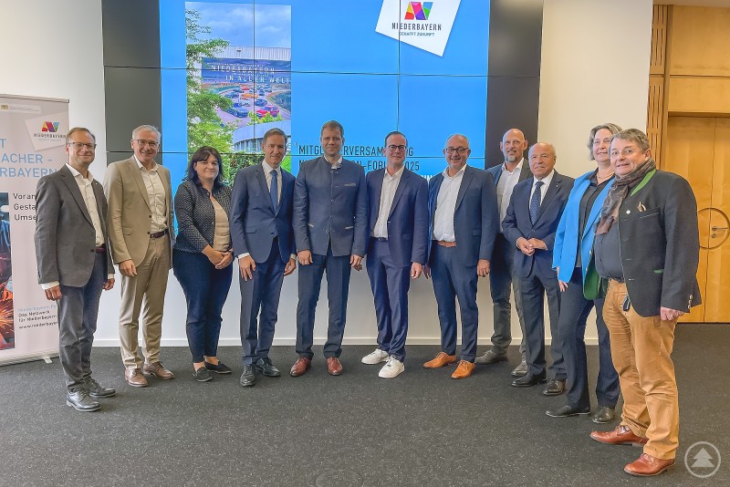 Eine Gruppe von zwölf Personen, darunter Vertreter aus Politik, Wirtschaft und Institutionen, steht nebeneinander vor einer großen Videowand mit dem Logo „Niederbayern-Forum“ und einem Bild des BMW-Werks.