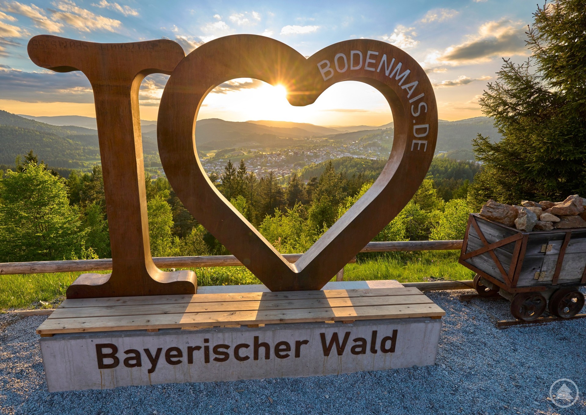 Ein neuer Fotospot in Bodenmais: „I love Bodenmais im Bayerischen Wald“ – ein beliebtes Motiv für Erinnerungsfotos. Ein großer „I love Bodenmais“-Fotospot aus Cortenstahl mit Blick auf eine idyllische Landschaft des Bayerischen Waldes. Der Sonnenuntergang scheint durch das Herz.
